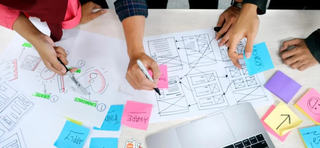 A imagem captura um momento de brainstorming, onde um grupo de pessoas discute, provavelmente, o Rebranding. A presença de esboços, fluxogramas e anotações coloridas sugere que eles estão no processo de redesenho da identidade visual da marca,