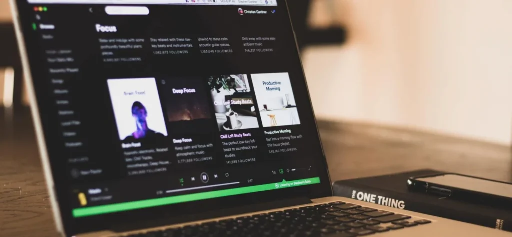 A imagem mostra um laptop exibindo o Spotify, uma plataforma que oferece uma vasta biblioteca musical. Para empresas que utilizam músicas em suas operações, entender o conceito de Royalty free.